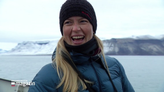 Eine warm gekleidete Frau auf einem Schiff im Nordpolarmeer lacht während eines Interviews. © Screenshot 