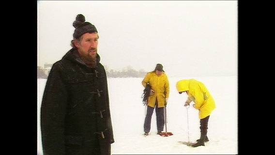 Eine alte Filmaufnahme von 1985: Ein Mann steht auf der zugefrorenen Alster während zwei Personen im Hintergrund die Dicke des Eises messen. © Screenshot 