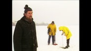 Eine alte Filmaufnahme von 1985: Ein Mann steht auf der zugefrorenen Alster während zwei Personen im Hintergrund die Dicke des Eises messen. © Screenshot 