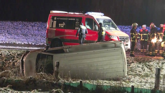 Ein weißer Transporter liegt in einem Straßengraben, dahinter sind ein Krankenwagen und Feuerwehrleute zu sehen. © Screenshot 