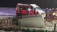 Ein weißer Transporter liegt in einem Straßengraben, dahinter sind ein Krankenwagen und Feuerwehrleute zu sehen. © Screenshot 