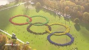 Menschen bilden auf einer Wiese die olympischen Ringe. © Screenshot 