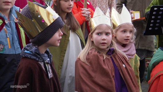 Drei kleine Sternsinger und Sternsingerinnen sammeln Spenden. © Screenshot 