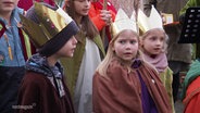 Drei kleine Sternsinger und Sternsingerinnen sammeln Spenden. © Screenshot 