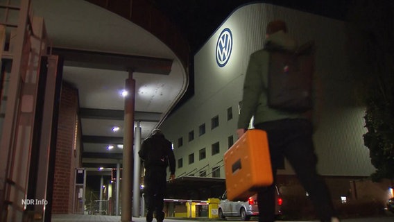 Menschen gehen im Dunkeln an einem Volkswagen-Werk vorbei. © Screenshot 