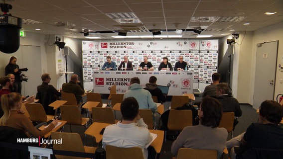 Eine Gruppe von Menschen sitzt hinter einem Tisch auf einer Pressekonferenz. © Screenshot 