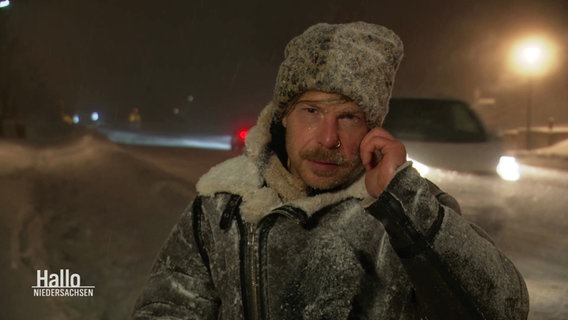 Reporter Tino Nowitzki mit eingeschneiter Jacke, Mütze und Mikrofon draußen vor Ort im Harz. © Screenshot 