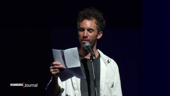 Poetry-Slammer Julian Heun steht beim vortragen eines Textes vor einem Stand-Mikrofon auf der Bühne. © Screenshot 