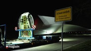 Ein riesiges Rotorblatt eines Windkraftwerks wird durch einen kleinen Ort bei Nacht transportiert. © Screenshot 