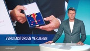 Nachrichtensprecher Robert Holm im Studio, links von ihm ein Bild eines Bundesverdienstkreuzes und die Unterschrift: "Verdienstorden verliehen". © Screenshot 