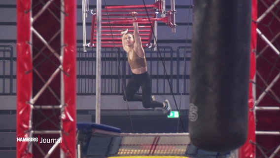 Beim Ninja Warriors Turnier in Hamburg: Eine Frau hangelt sich an einer Sprossenwand entlang. © Screenshot 