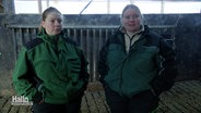 Die Landwirtinnen Laura und Marike Allers stehen in Arbeitskleidung nebeneinander im Stall. © Screenshot 