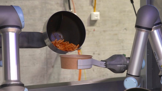 Ein Roboter schüttet eine Pasta in einen Behälter. © Screenshot 