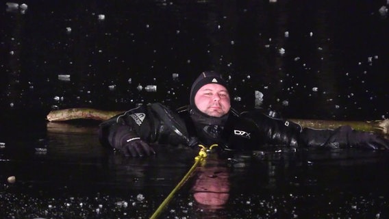 Ein Taucher guckt aus einem Loch in einer Eisfläche. © Screenshot 