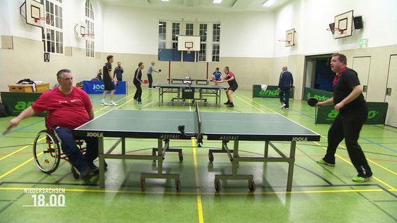 Zwei Männer, davon sitzt einer im Rollstuhl, spielen in einer Turnhalle Tischtennis. © Screenshot 