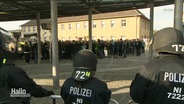 Einsatzkräfte der Polizei stehen bei einem Fan-Aufmarsch in Schutzausrüstung einer größeren Menschenmasse gegenüber. © Screenshot 