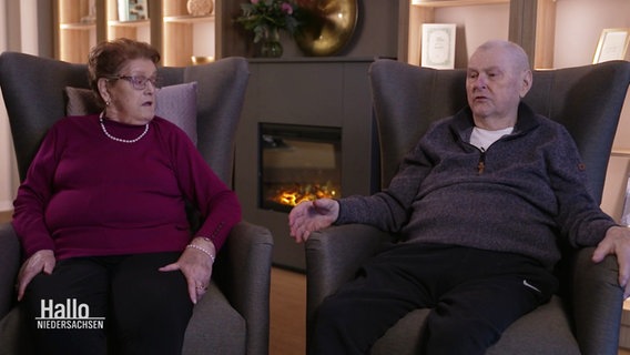 Das Ehepaar Eleonore und Wilhelm Deseniß sitzt in Ohrensesseln vor einem Kamin. © Screenshot 