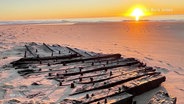 Ein im Strand halb vergrabenes Schiffswrack bei Sonnenuntergang © Screenshot 