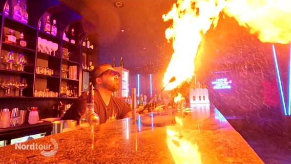 Ein Barkeeper spukt an einer Theke Feuer. © Screenshot 