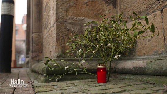 An der Außenwahnd einer Kirche lehnt ein Mistelzweig und eine rote Grabkerze. © Screenshot 