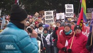 Ein Mann hält eine Ansprache vor einer größeren Menschenmenge mit Plakaten bei einer Kundgebung gegen Rechtsextremismus. © Screenshot 