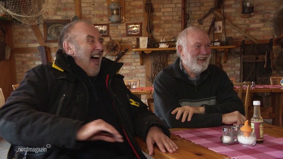 Zwei ältere Männer sitzen an einem Tisch und lachen. © Screenshot 