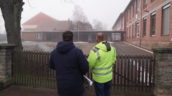 Samtgemeindebürgermeister Philipp Ralphs und Bauamtsleiter Michael Kaminsky schauen auf den Schulhof der Grundschule in Heeseberg. © Screenshot 