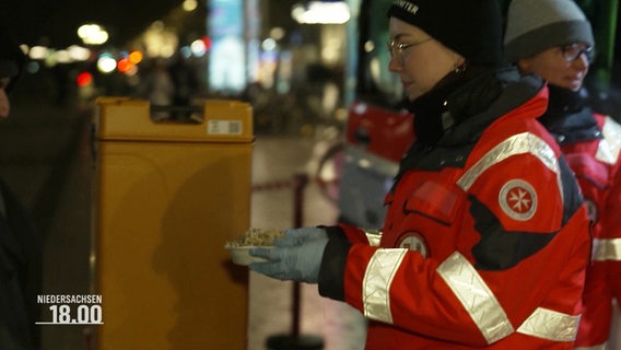 Eine Frau der Hilfsorganisation Malteser verteilt Essen an Obdachlose. © Screenshot 