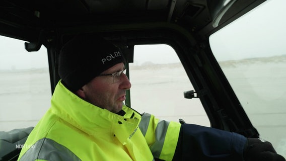 Ein Polizeibeamter in einem Fahrzeug am Strand. © Screenshot 