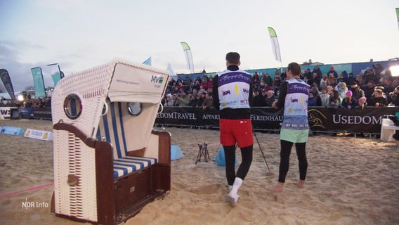 Zwei Männer neben einem Strandkorb vor Publikum. © Screenshot 