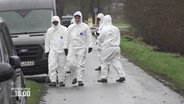 Menschen in weißen Schutzanzügen auf einem kleineren asphaltierten Feldweg bei Nieselregen © Screenshot 