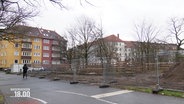 Neben einer Straße in einem Wohngebiet wird auf einem abgezäunten Gebiet ein kleiner Wald mit einigen kleineren Bäumen gepflanzt. © Screenshot 