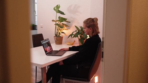 Eine junge Frau sitzt vor einem aufgeklappten Laptop an einem Tisch bei einem Video-Anruf. © Screenshot 