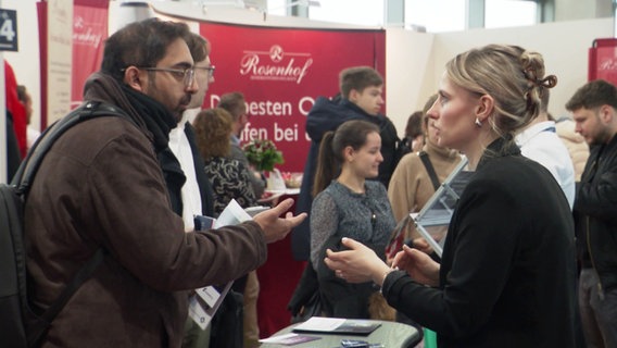 Menschen unterhalten sich auf einer gut besuchten Jobmesse. © Screenshot 