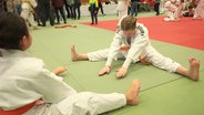 Ein Mädchen im Judo-Anzug dehnt sich auf einer Matte. © Screenshot 