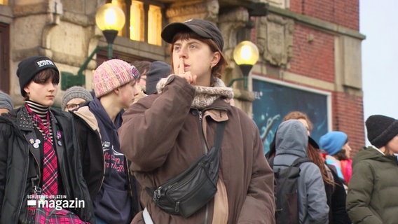 Junge Menschen bei einer Demonstration. Eine junge Frau legt zum Zeichen für Stille den Finger an die Lippen. © Screenshot 