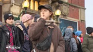 Junge Menschen bei einer Demonstration. Eine junge Frau legt zum Zeichen für Stille den Finger an die Lippen. © Screenshot 