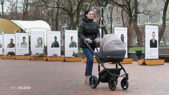 Eine Frau schiebt einen Kinderwagen über einen Platz. © Screenshot 