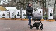 Eine Frau schiebt einen Kinderwagen über einen Platz. © Screenshot 