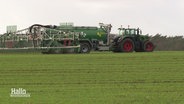 Ein Traktor fährt mit einem Düngemittel-Anhänger über ein Feld. © Screenshot 