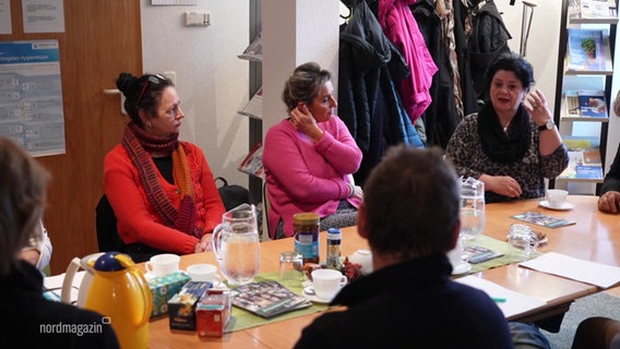 Bei einer Selbsthilfegruppe sitzen mehrere Menschen in einem Gemeinschaftsraum an einem Tisch. © Screenshot 