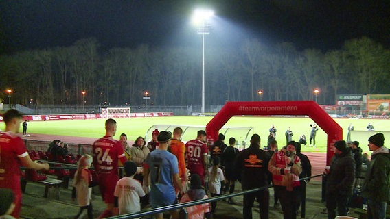 .Die neue Flutlichtanlage im Greifswalder Volksstadion leuchtet als die Mannschaft des GFC auf den Platz läuft. Die Spieler und Ballkinder sind von hinten zu sehen vor dem erleuchteten Nachthimmel. © Screenshot 