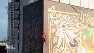 Ein Fassadenkletterer bringt am Turm der Martktkirche in Hannover ein großes Banner an. © Screenshot 