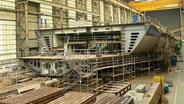 Ein noch nicht fertig gebautes Schiff in einer Werft. © Screenshot 