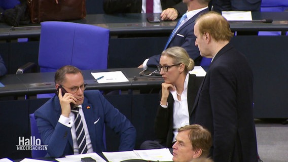 Blick in den Bundestag. AfD-Politiker Tino Chrupalla sitzt auf seinem Platz mit ernsten Gesicht und dem Handy am Ohr. © Screenshot 