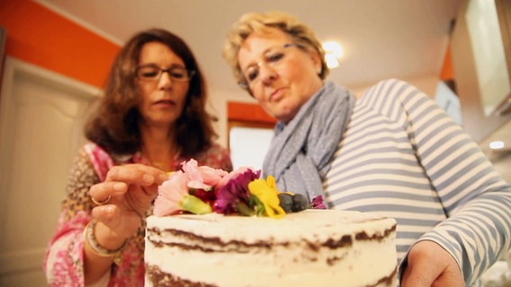 Zwei Frauen verzieren eine Torte mit Blumen. © Screenshot 