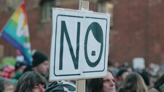 Ein Protestschild mit der Aufschrift: "NO" Das "O" ist mit Seitenscheitel und Hitlerbärtchen dekoriert. © Screenshot 