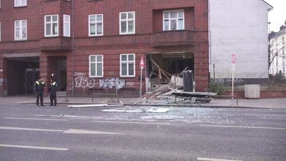 Zwei Polizisten stehen neben dem Gebäude wo die Explosion stattfand. Zu sehen ist ein komplett herausgerissenes  Fenster. © Screenshot 