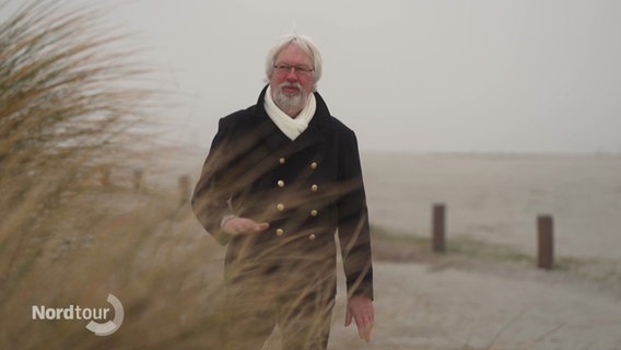 Ein Mann geht an einer Sanddüne an einem Strand entlang. © Screenshot 