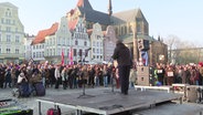 Bei einer Demonstration hören viele Menschen einer Person bei ihrer Rede auf einem Marktplatz zu. © Screenshot 